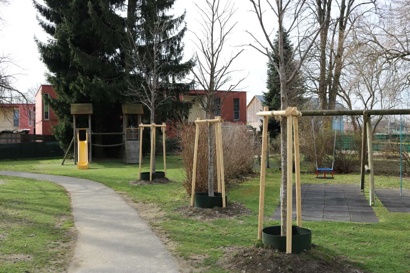 Zu sehen ist: eine Wiese in einem Kindergarten mit neu eingepflanzten Bäumen