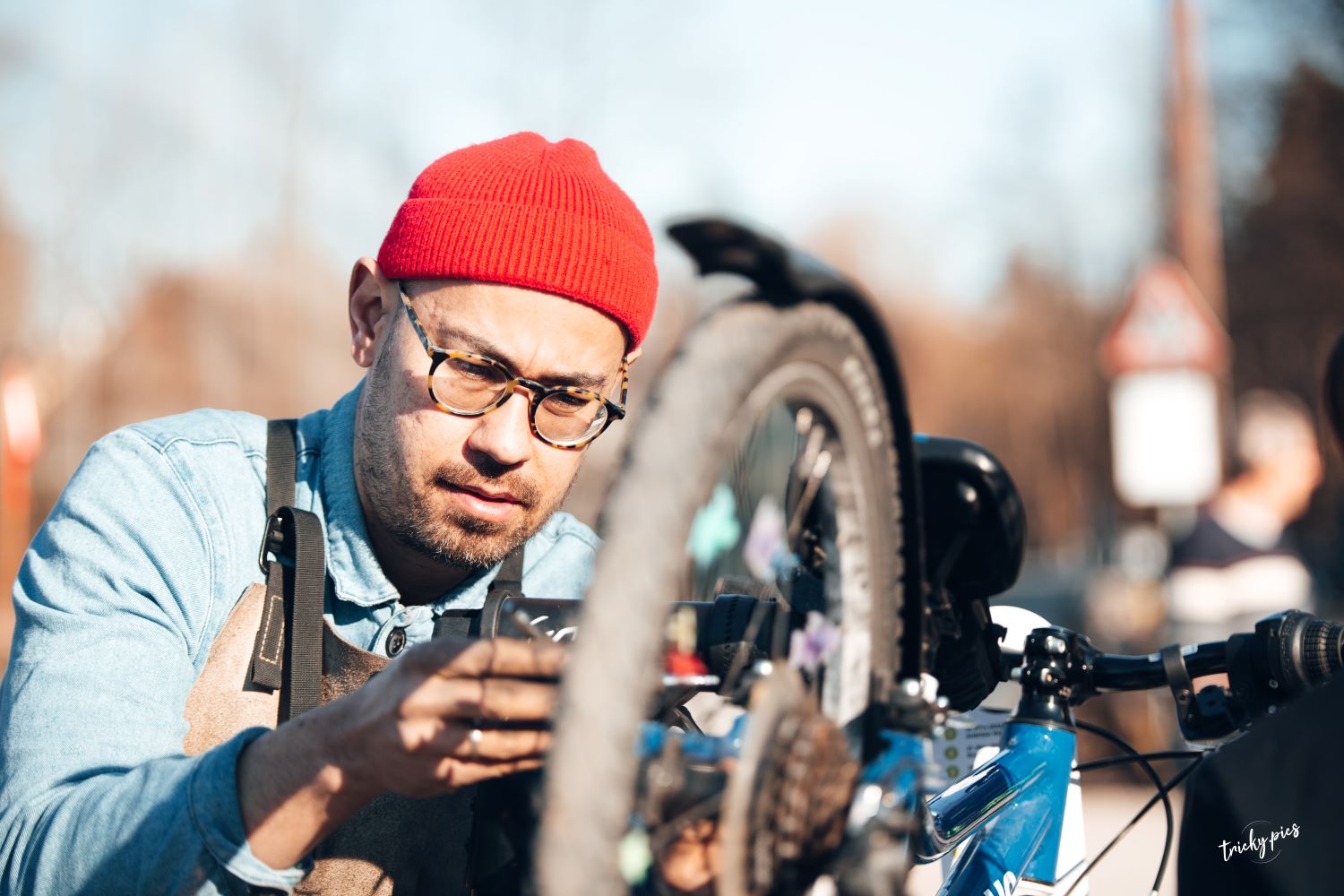 Zu sehen ist: ein Herr mit Brille und roter Mütze repariert ein Fahrrad.
