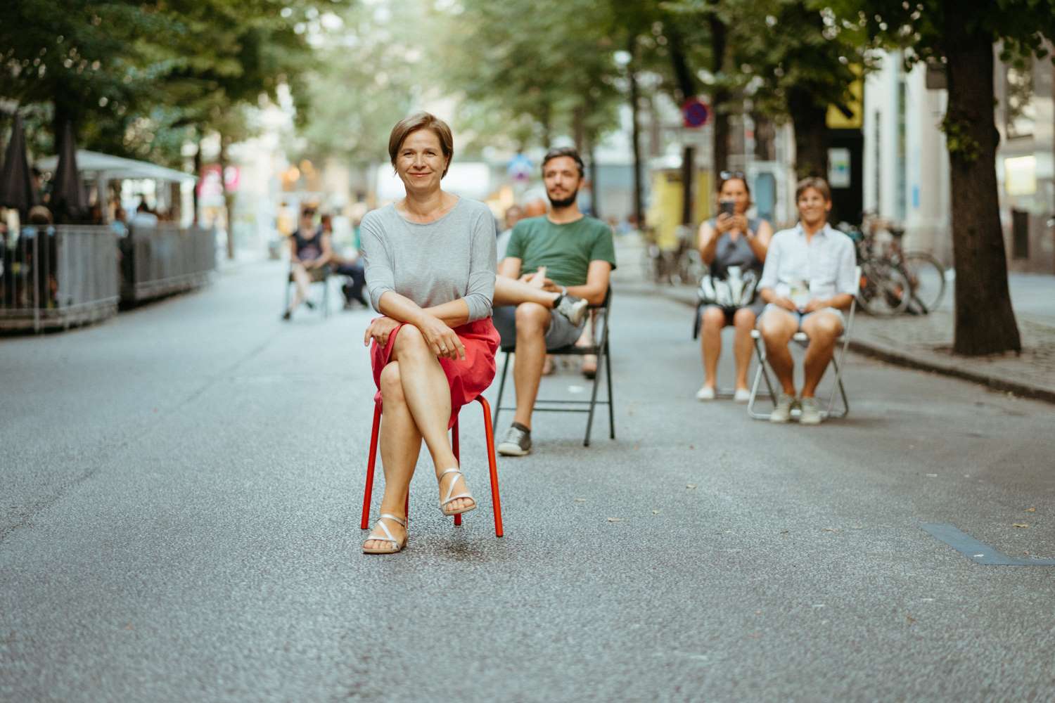 Zu sehen sind: Judith Schwentner und weitere Personen sitzen in einer begrünten Straße in Graz
