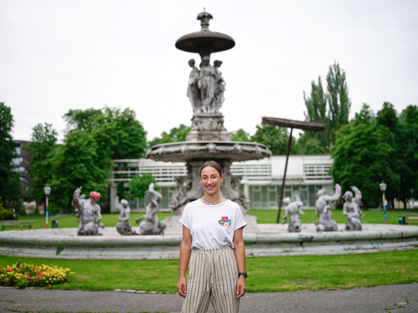 Zu sehen ist: eine Person vor einem Brunnen in einem Park