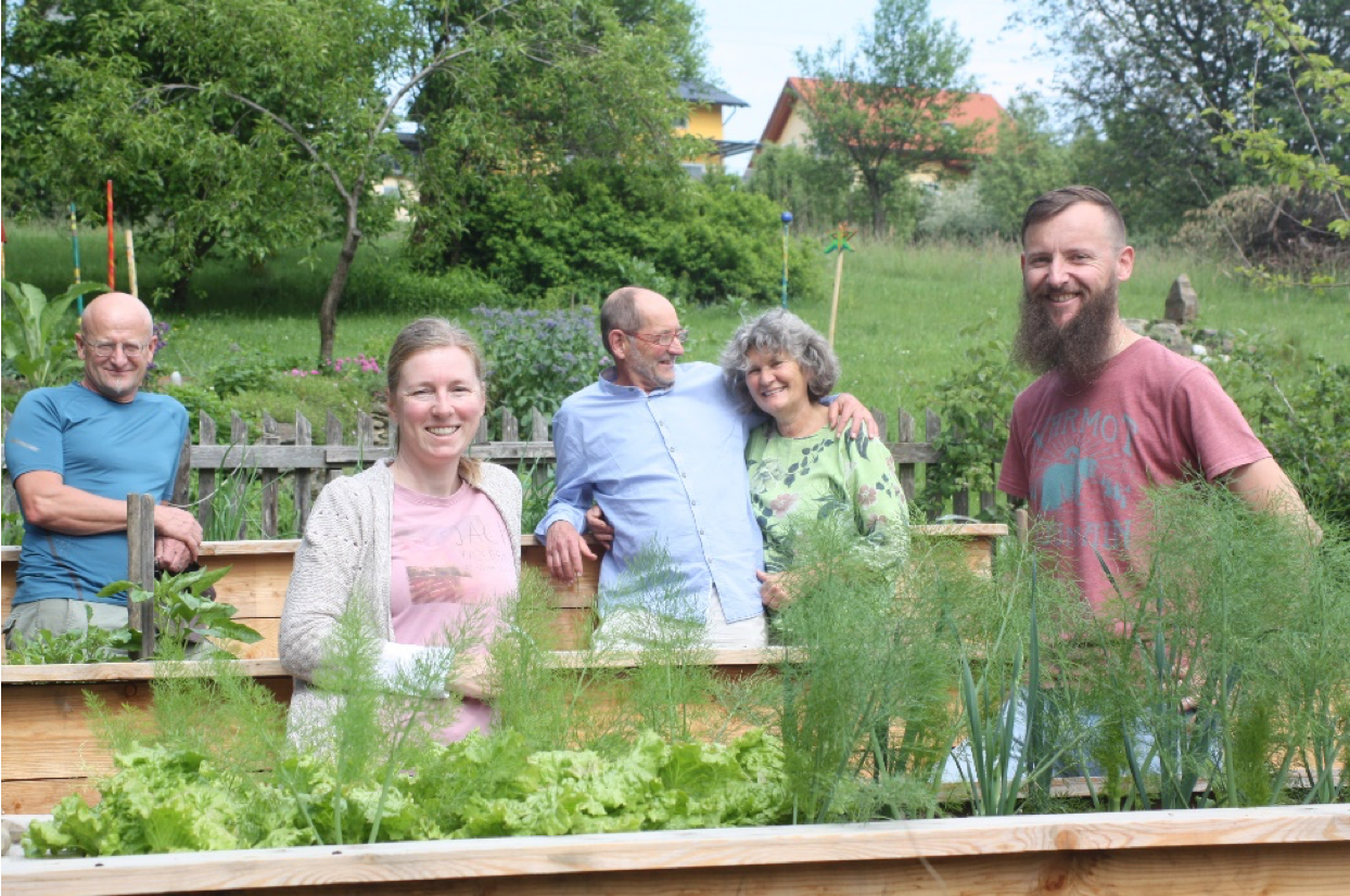 Auf diesem Bild sind die Mitglieder der Grünen Gemeindegruppe in Söding-St. Johann zu sehen, die alle in einem Gemeinschaftsgarten mit Hochbeeten stehen und in die Kamera lächeln.